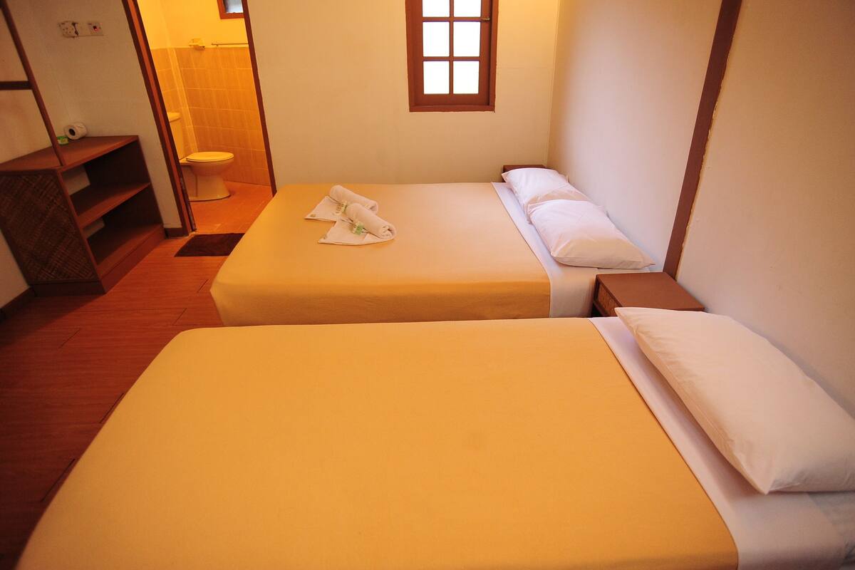 Une chambre d’hôtel avec deux lits, une petite fenêtre et une salle de bain visible au fond.