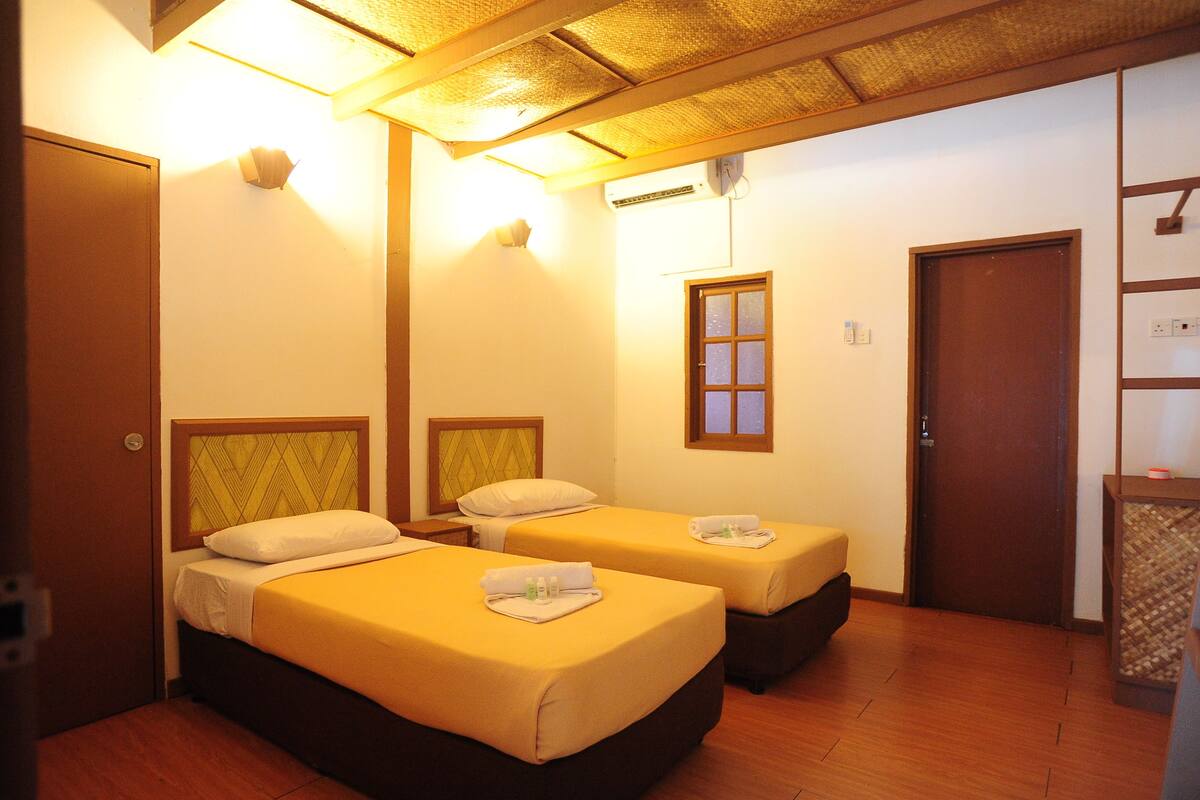 Une chambre d’hôtel avec deux lits, un plancher en bois, une porte en bois et une petite table avec un panier.