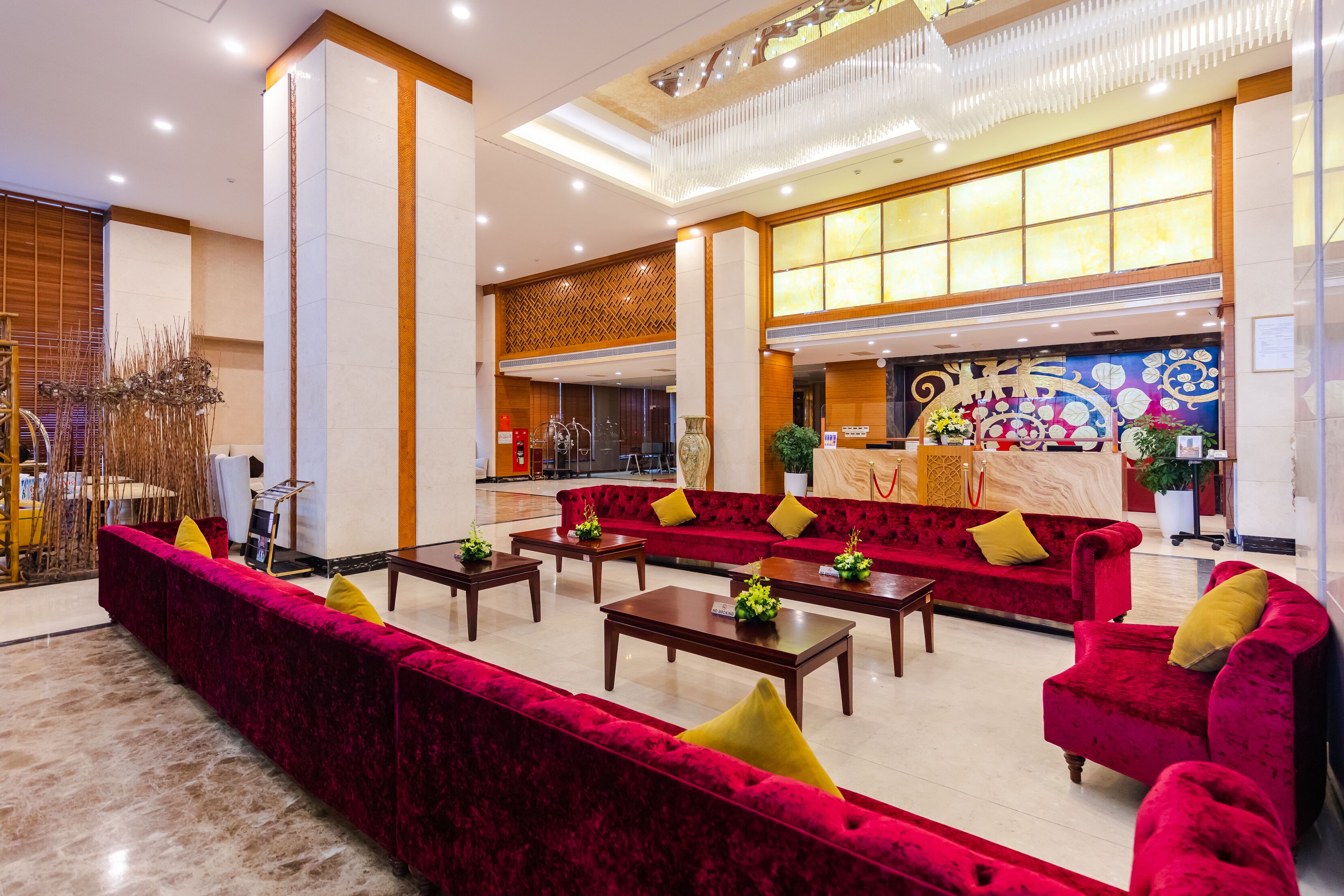 A spacious lobby with red velvet sofas, wooden tables, and a decorative wall.