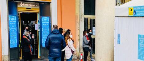 A pharmacy named 'Farmacia Longo' with a tiled entrance and people queuing outside.