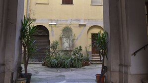 A courtyard with potted plants, a central fountain, and a building with arched doorways. - B&B La Casa di Patty (Rome)