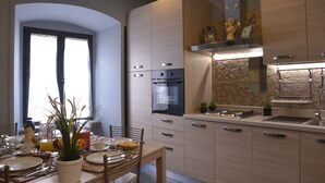 A modern kitchen with built-in appliances, a dining area with a table set for two, and a stone accent wall. - B&B La Casa di Patty (Rome)