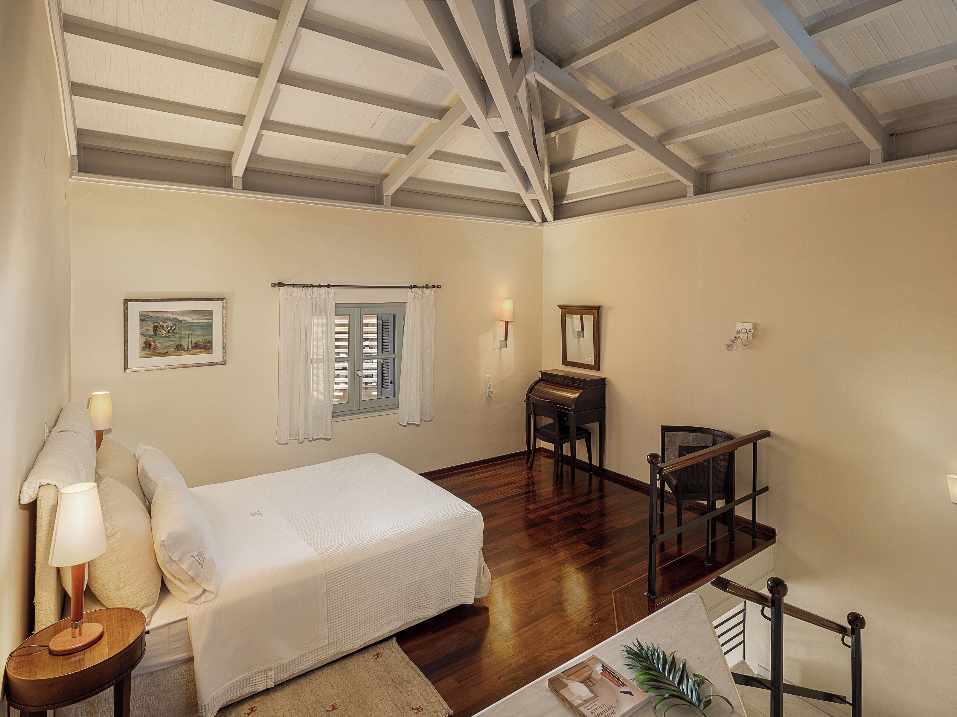 A bedroom with a bed, a desk, a chair, a lamp, a window with curtains, a painting, and a staircase.