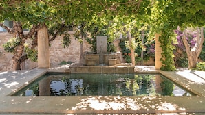 A pool with a stone fountain, surrounded by trees and a stone wall. - Villa Andromeda (Chania)