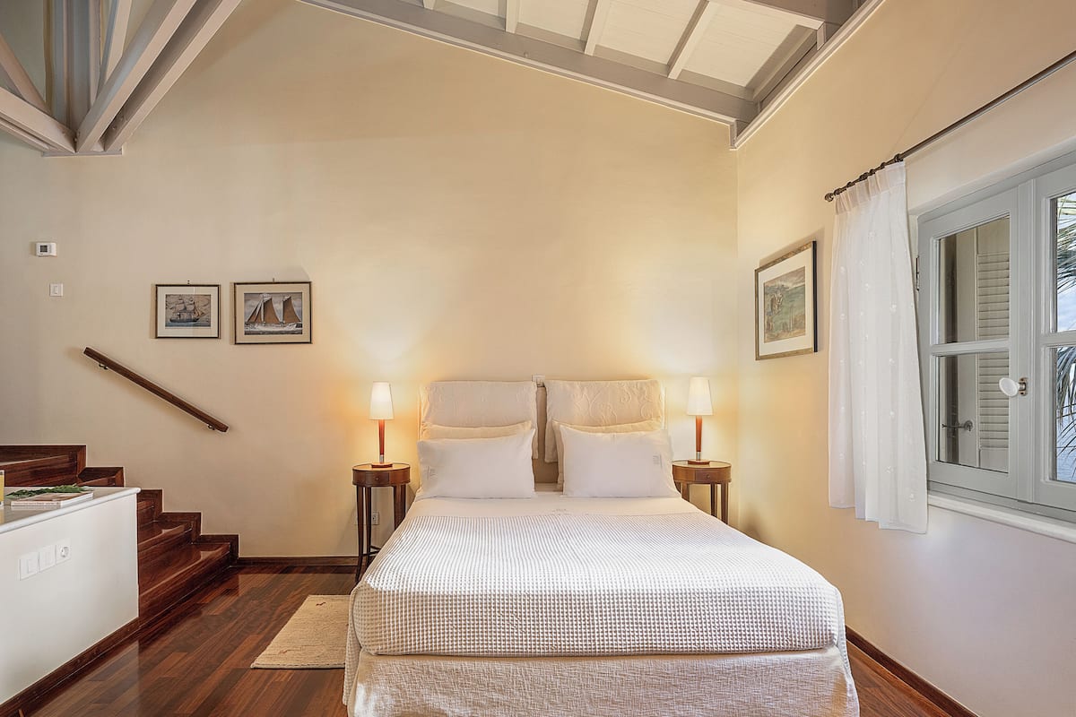 Un dormitorio con una cama grande, dos mesitas de noche con lámparas, una escalera de madera y cuadros enmarcados en la pared.