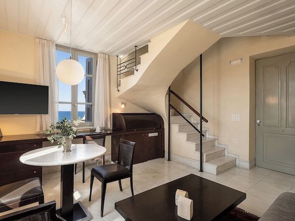 A modern living room with a large TV, a round dining table, a sofa, and a staircase. - Villa Andromeda (Chania)