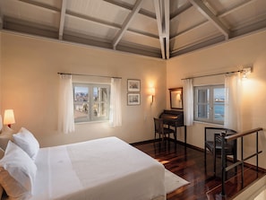 A hotel room with a bed, a desk, a chair, and a view of the sea through the windows. - Villa Andromeda (Chania)