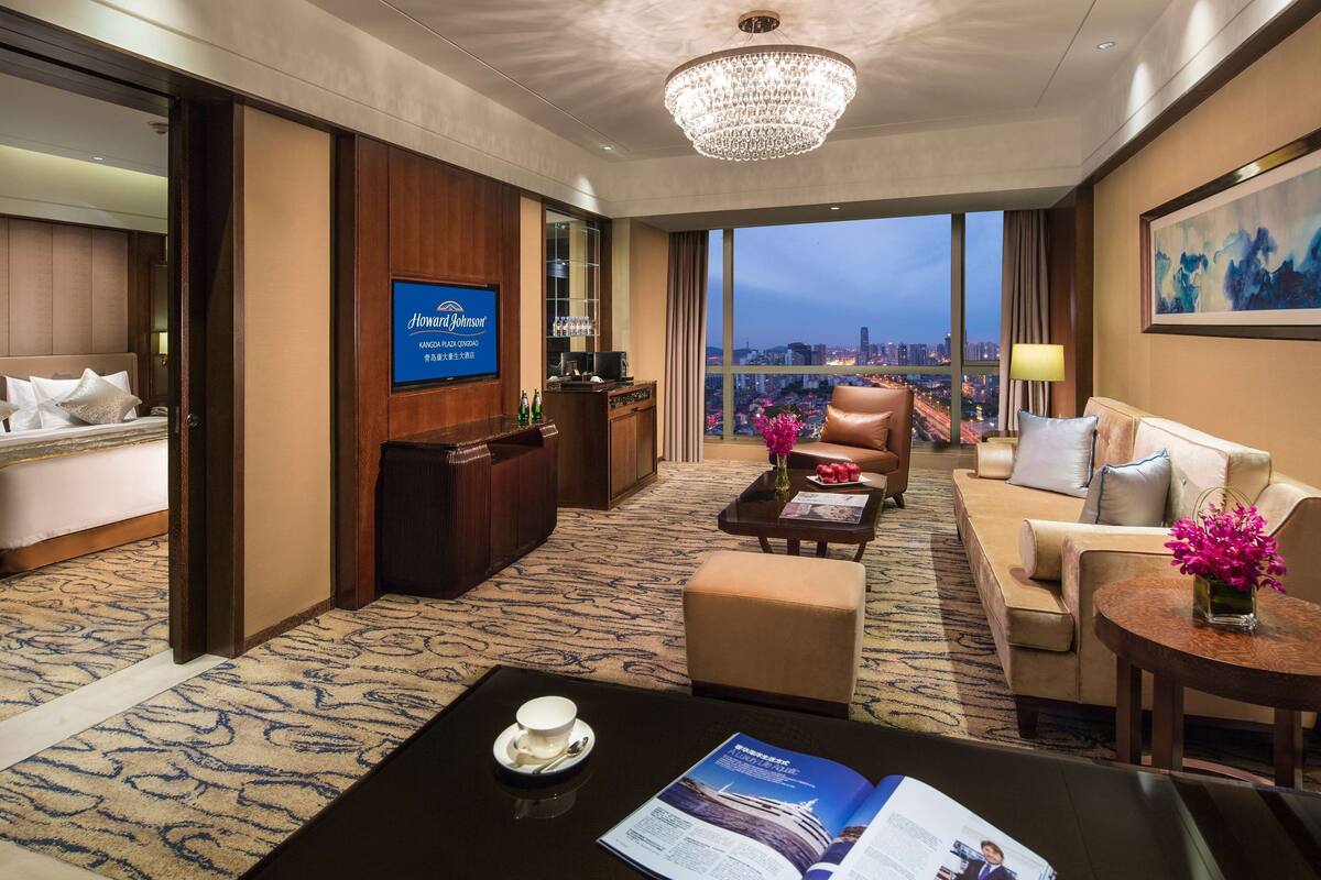 Habitación de hotel con vistas a la ciudad, una zona de bar, una sala de estar con una mesa de centro y una cama con almohadas.