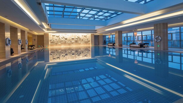 En rummelig indendørs swimmingpool med glasloft, moderne design og et siddeområde med udsigt til himlen.