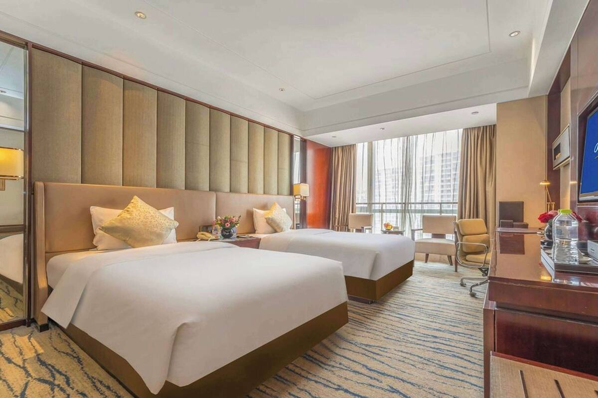 Habitación de hotel con dos camas, un escritorio, televisor y un ventanal con cortinas.