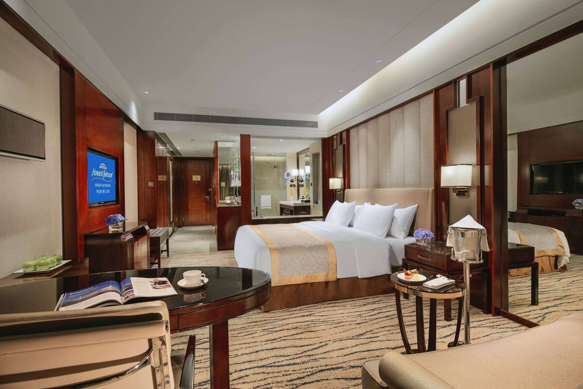 Habitación de hotel con una cama grande, un escritorio con silla, televisor y baño visible a través de una puerta abierta.