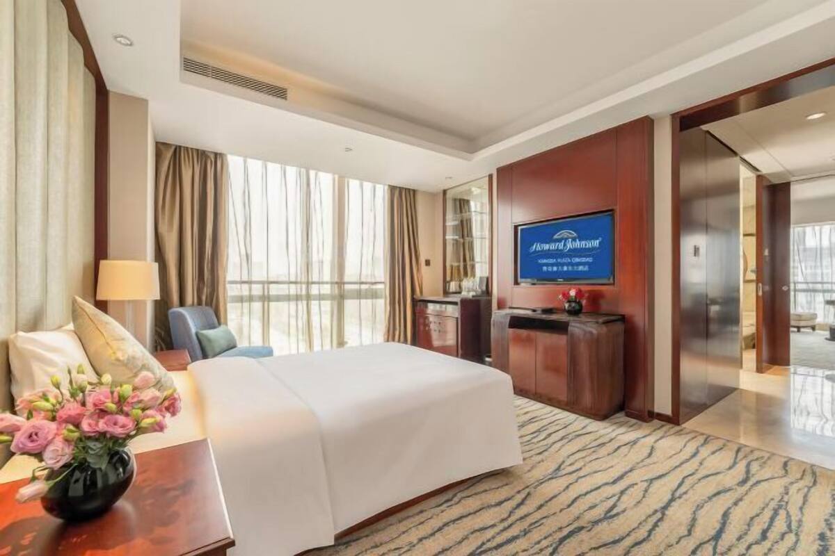 Habitación de hotel con cama, escritorio, televisión y vistas al exterior.