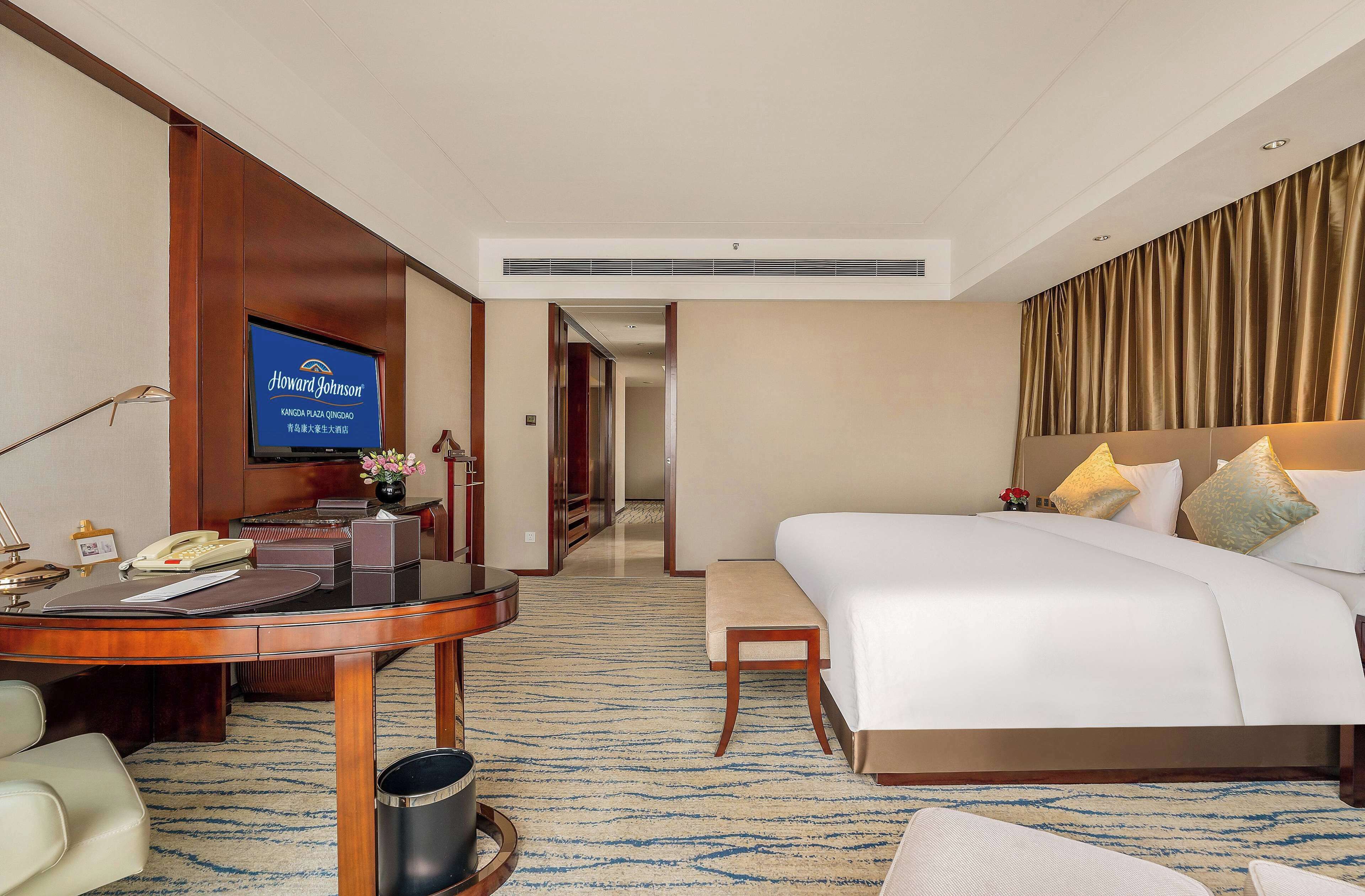 A hotel room with a bed, a desk with a telephone, a television, and a carpeted floor.