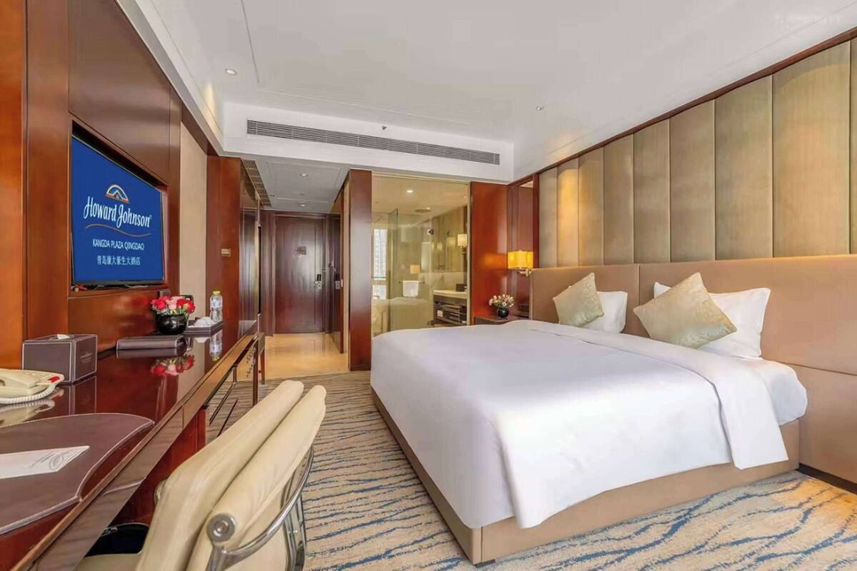 Una habitación de hotel con una cama grande, un escritorio con teléfono y un televisor que muestra el nombre del hotel.