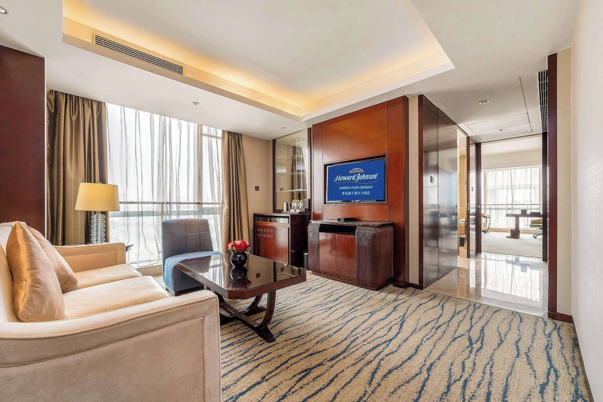 Habitación de hotel con sofá, una mesa de centro, televisor y vistas al exterior.