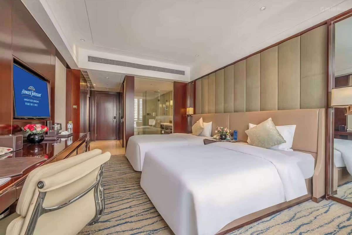 Habitación de hotel con dos camas, un escritorio, una silla y un televisor.