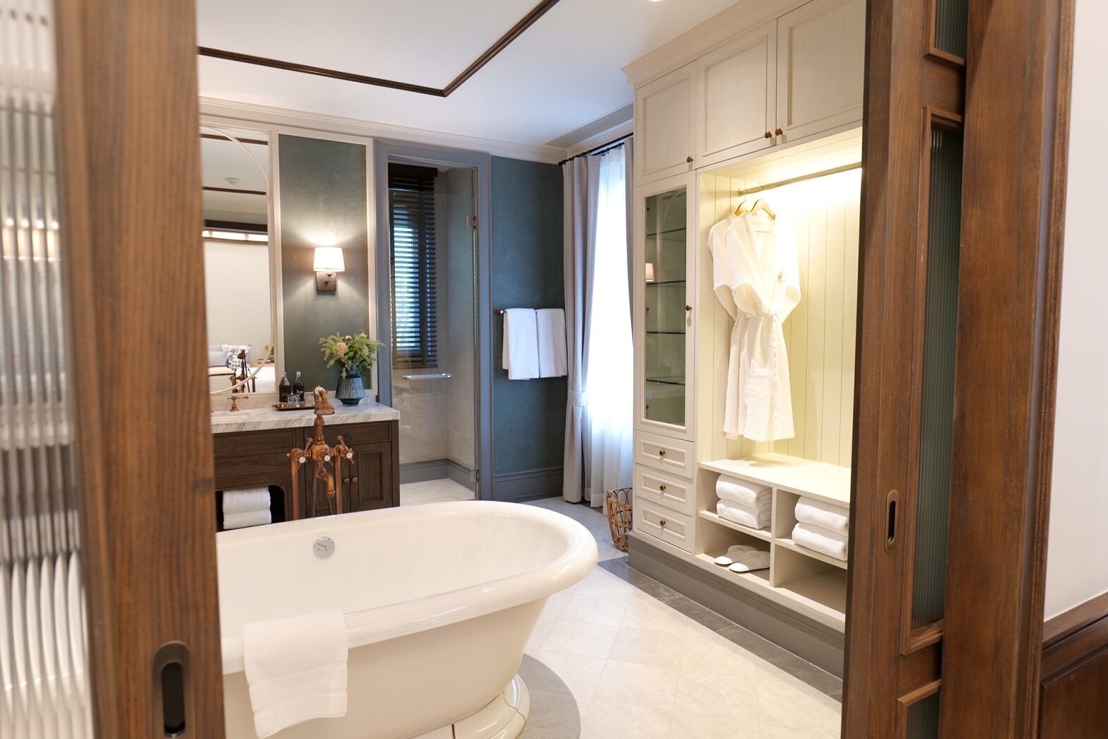 A modern bathroom with a freestanding bathtub, a vanity with a mirror, and a walk-in closet with hanging robes.