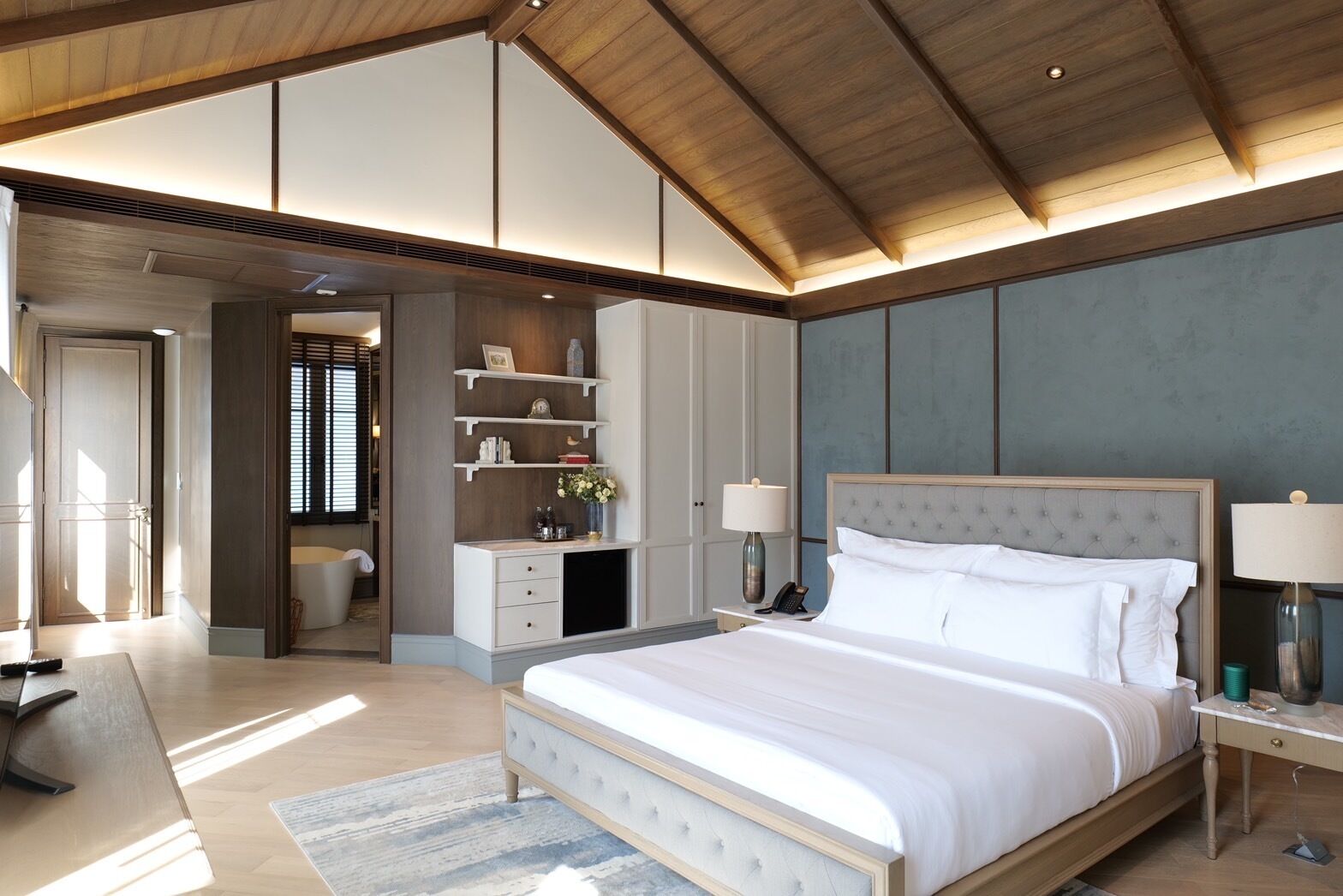 A spacious bedroom with a large bed, built-in shelving, and a wooden ceiling.