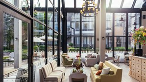 Un intérieur spacieux doté de grandes fenêtres, un espace de détente central avec des canapés et des fauteuils, et un coin repas avec des tables et des parasols.
