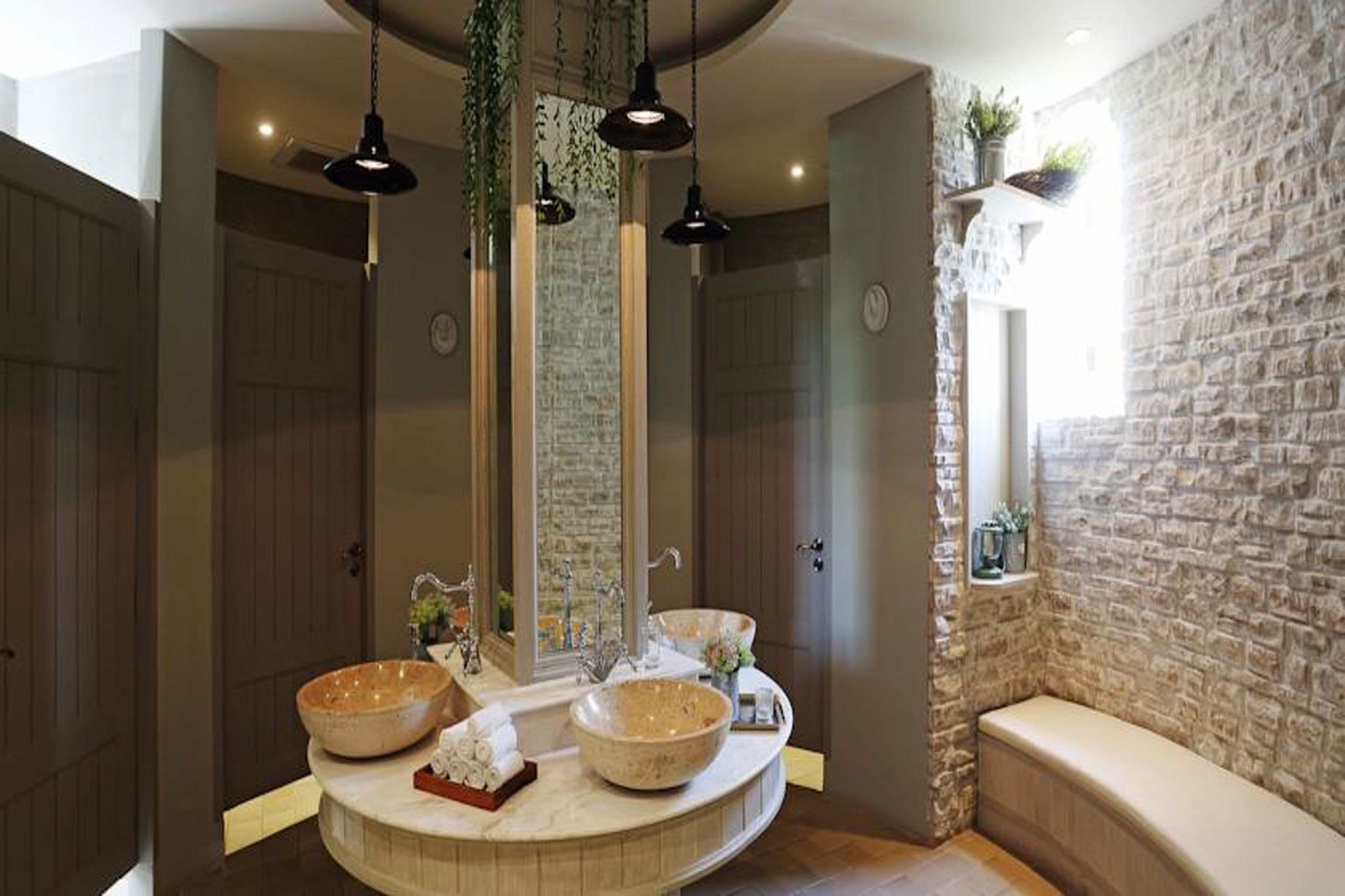 A bathroom with a round vanity, two large bowls, a mirror, and a stone wall.
