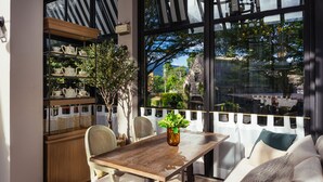 Un coin repas avec une table en bois, des chaises et un canapé. On y trouve une étagère avec des services à thé et une plante en pot.