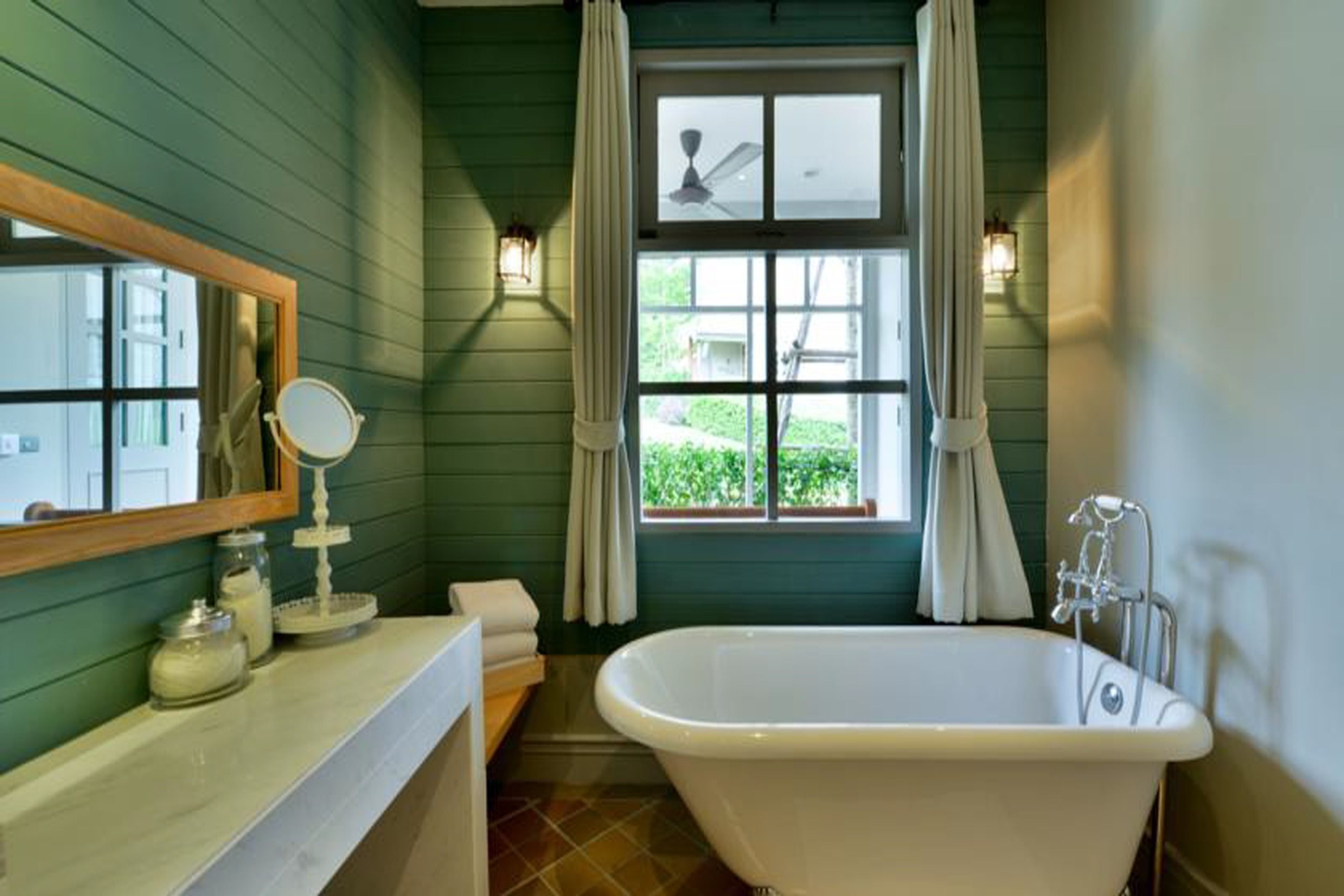 A bathroom with a freestanding bathtub, a vanity with a mirror, and a window with curtains.