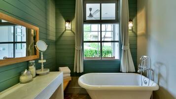 A bathroom with a freestanding bathtub, a vanity with a mirror, and a window with curtains.