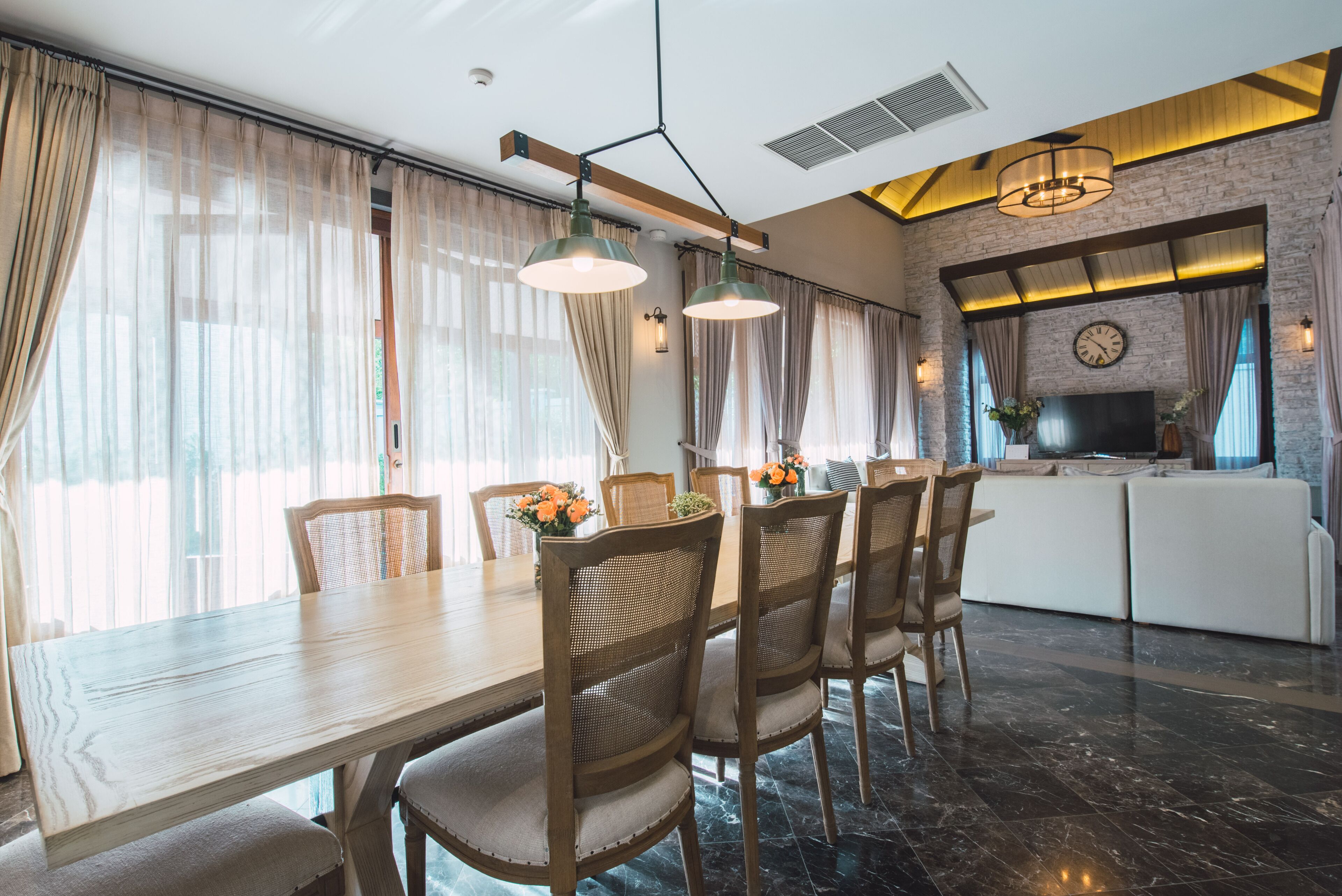 A modern dining area with a wooden table and wicker chairs, a kitchen with a large TV, and a brick accent wall.