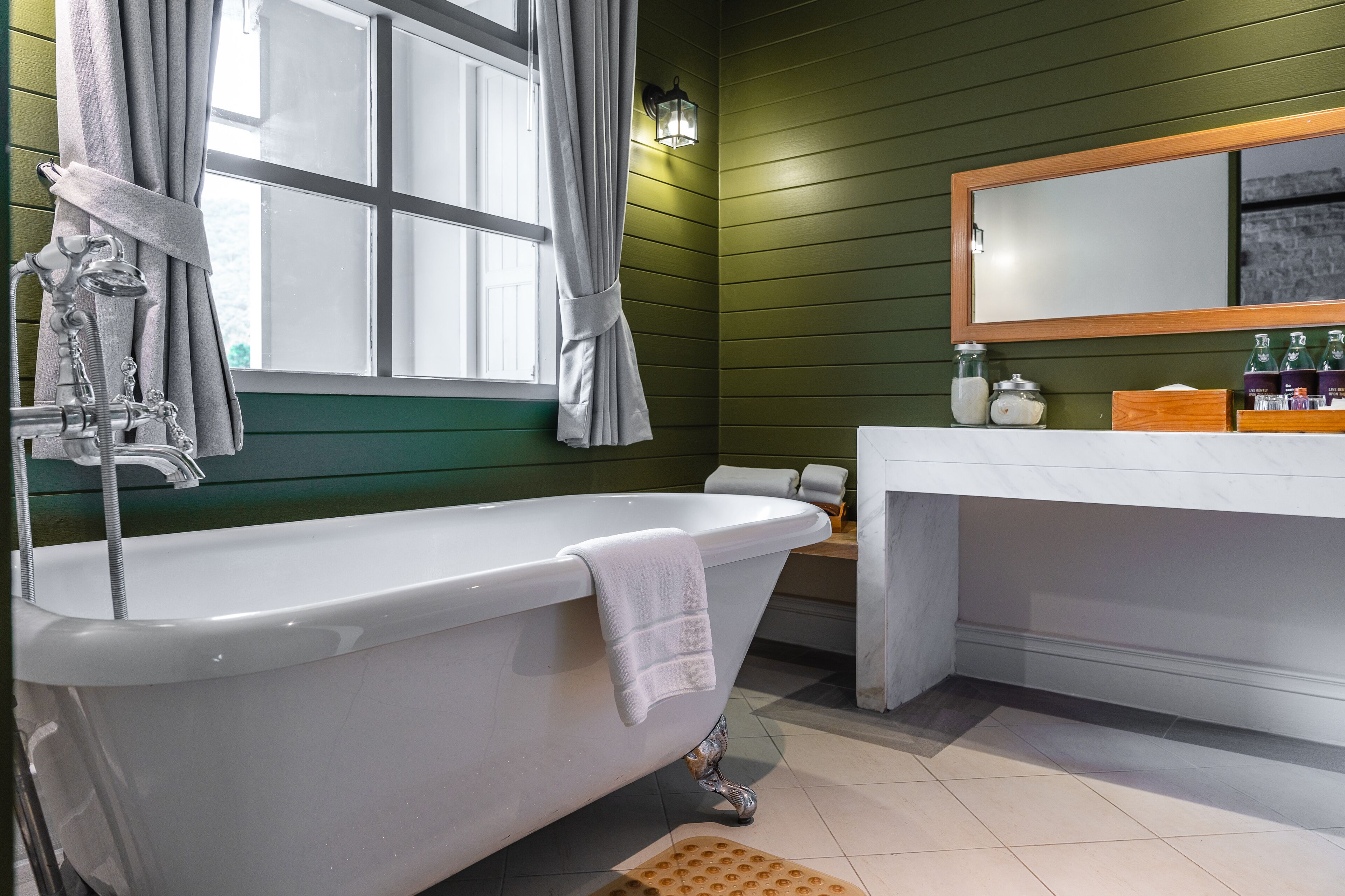 A bathroom with a freestanding bathtub, a vanity with a mirror, and a window with curtains.