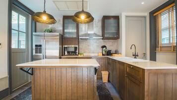 Une cuisine moderne avec des meubles en bois, un grand îlot central, des appareils en acier inoxydable et des luminaires suspendus.