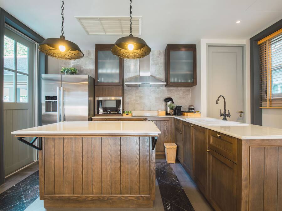 Une cuisine moderne avec des meubles en bois, un grand îlot central, des appareils en acier inoxydable et des luminaires suspendus.