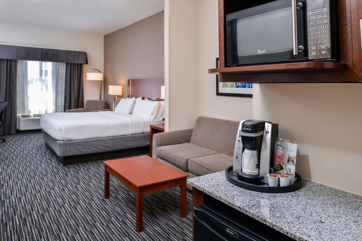 A hotel room with a bed, a sofa, a coffee maker, and a microwave.