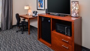 A hotel room with a wooden desk, a black refrigerator, a microwave, a black office chair, a desk lamp, and a framed abstract painting on the wall. - Holiday Inn Express & Suites York by IHG (York)