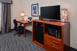 A hotel room with a wooden desk, a black refrigerator, a microwave, a black office chair, a desk lamp, and a framed abstract painting on the wall. - Holiday Inn Express & Suites York by IHG (York)