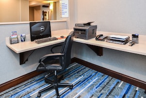 Um espaço de trabalho em hotel, com escrivaninha, computador, impressora e cadeira de escritório.