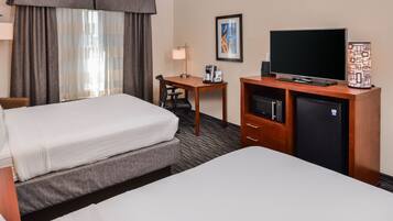 A hotel room with two beds, a desk, a television, a coffee maker, and a refrigerator.