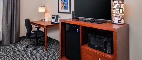 Ein Hotelzimmer mit Schreibtisch, Flachbildfernseher, Kaffeemaschine, Mikrowelle und einem Schrank mit Schubladen.
