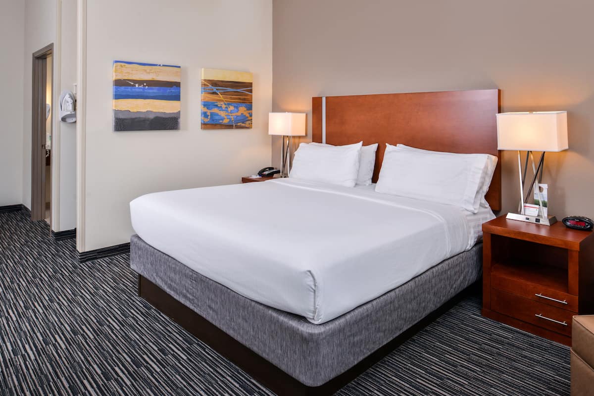 A hotel room with a large bed, two bedside tables, a nightstand, and a door.