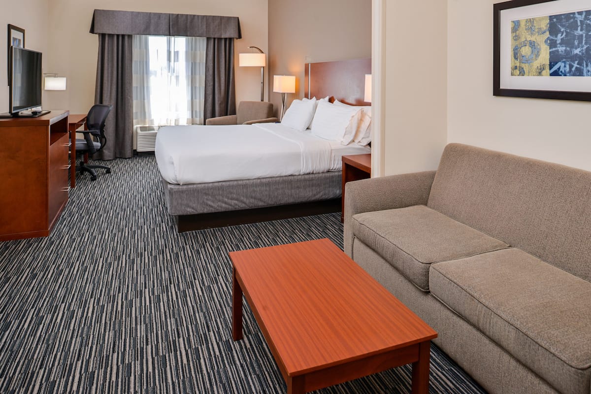 A hotel room with a bed, a sofa, a desk with a TV, a chair, and a lamp.