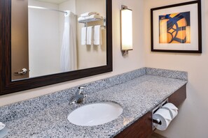 Une salle de bain avec un lavabo doté d’un plan de travail en granit, un miroir, un porte-serviettes et un tableau abstrait encadré.