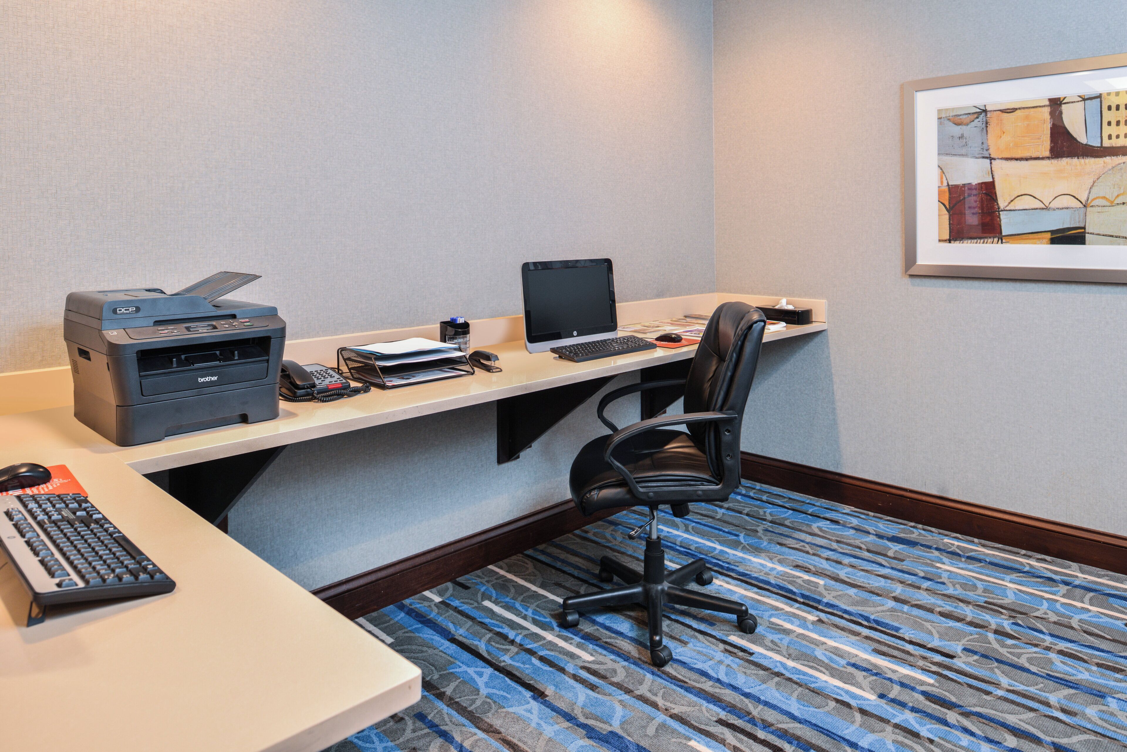 A hotel room with a desk, printer, computer, and a chair.