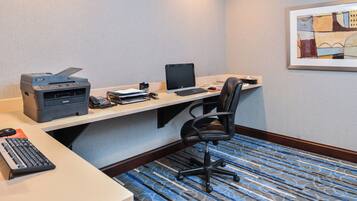 A hotel room with a desk, printer, computer, and a chair.