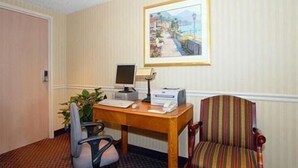 A hotel room with a desk, a striped armchair, a computer, and a framed painting on the wall.