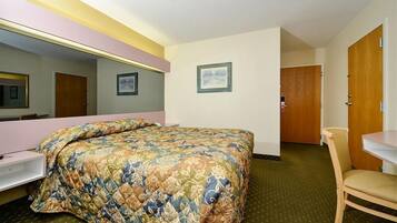 A hotel room with a bed, a chair, a desk, a mirror, and a door.