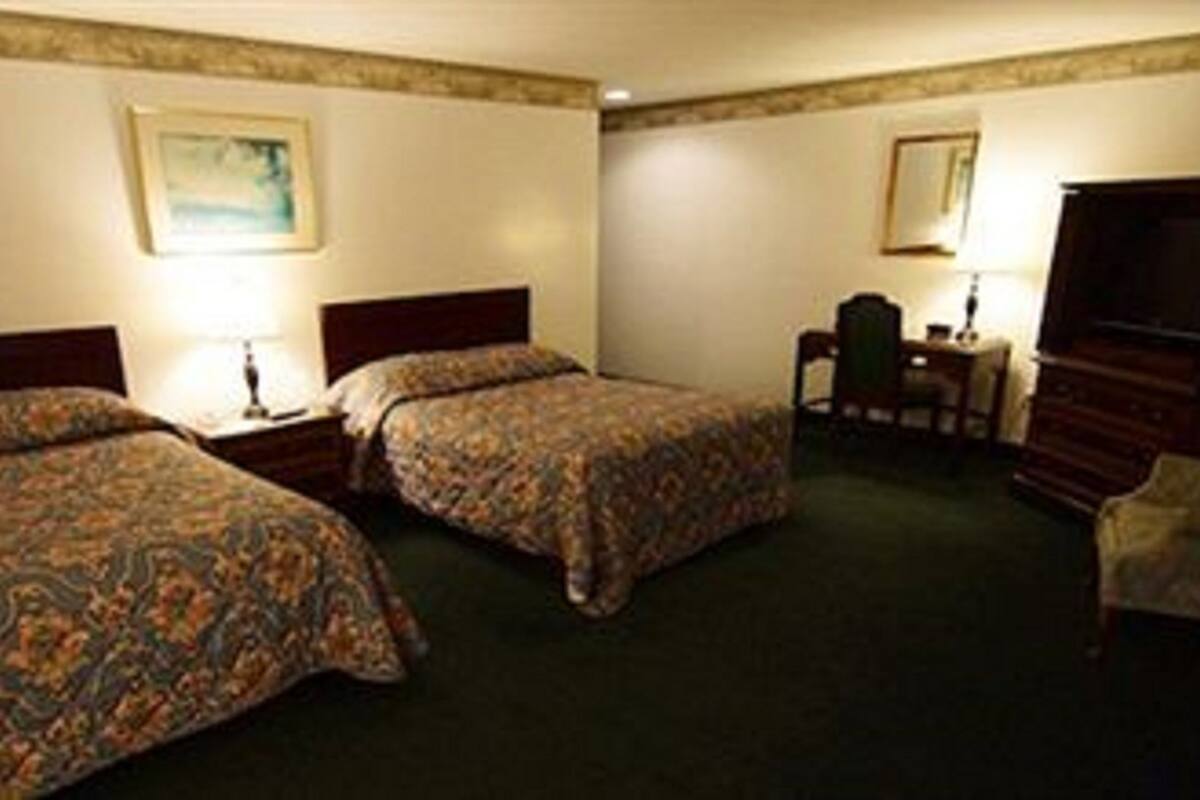 A hotel room with two beds, a desk, a chair, and a wardrobe.