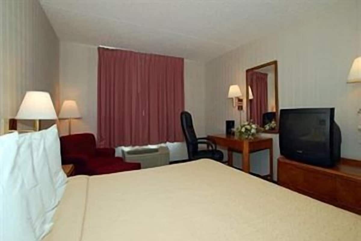 A hotel room with a bed, a desk with a television, a chair, a desk lamp, and a window with curtains.