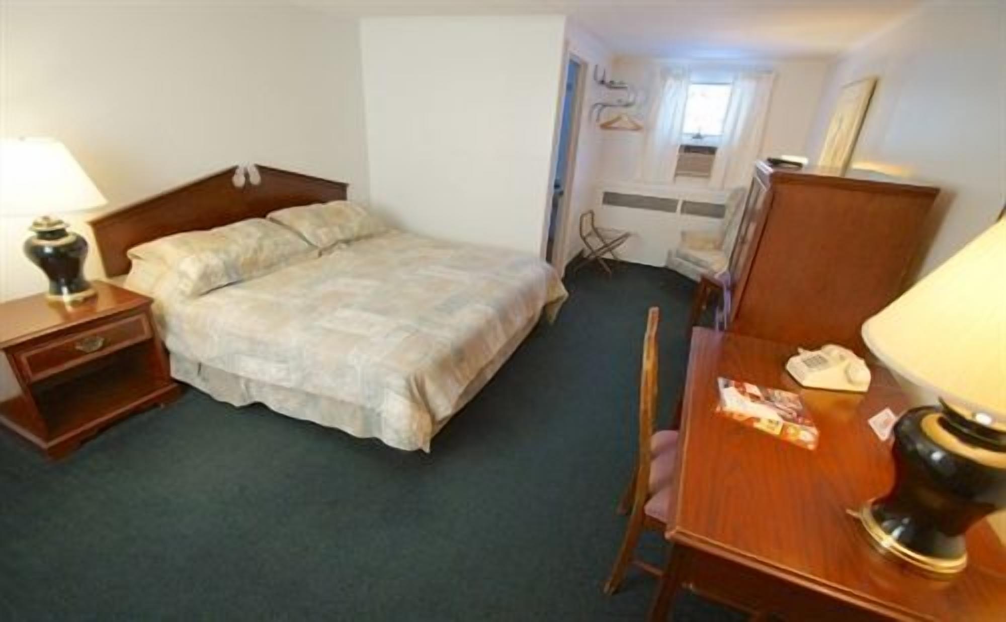 A hotel room with a bed, a desk, a chair, a lamp, a dresser, and a window.