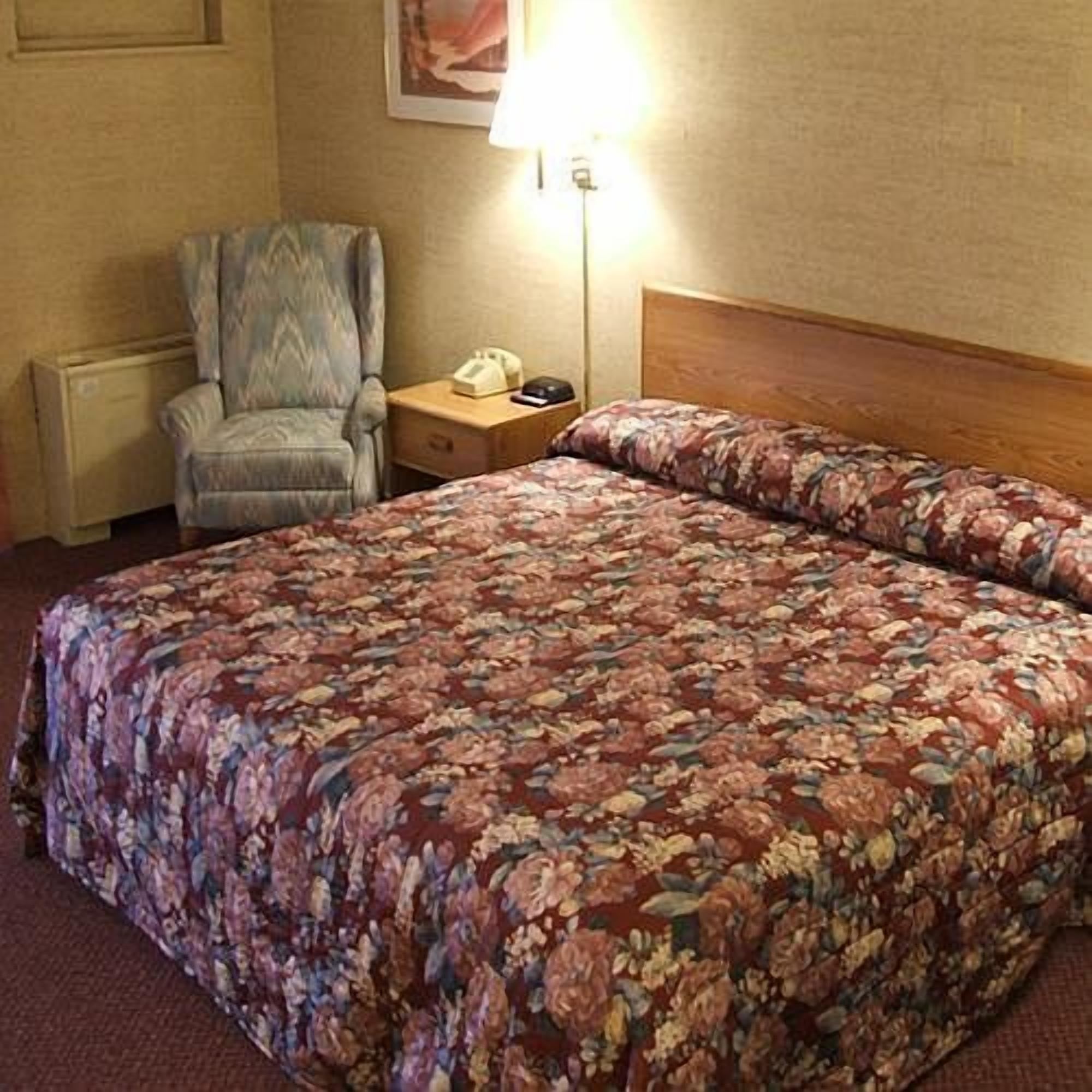 A hotel room with a large bed, a chair, a nightstand, and a lamp.