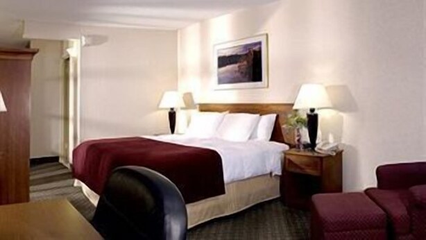 A hotel room with a bed, two bedside lamps, a nightstand, a chair, and a desk.