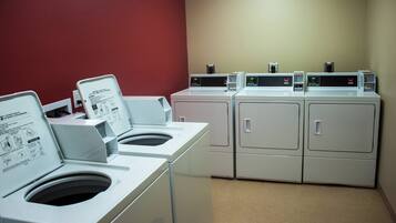 A laundry facility with multiple washing machines and dryers, a red wall, and a beige floor.